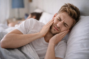 A guy feeling jaw pain in the bed, holding hand against cheeks