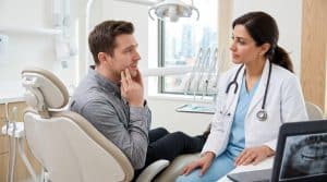Dentist talking with a male patient about recurring tooth pain in a consultation
